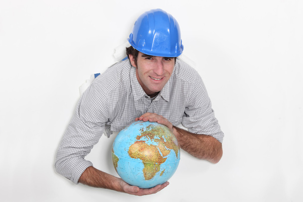 A construction worker holding a globe. - Фото, изображение