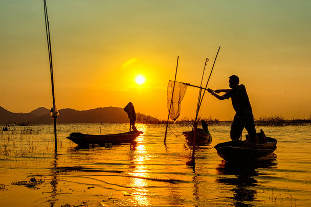 Sellaisten kalastajien siluetti, jotka käyttävät verkkoja kalojen pyytämiseen järvestä
 - Valokuva, kuva