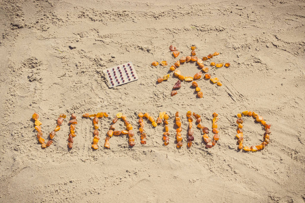 Medical pills, inscription vitamin D and shape of sun on sand at beach, summer time and healthy lifestyle - Fotó, kép