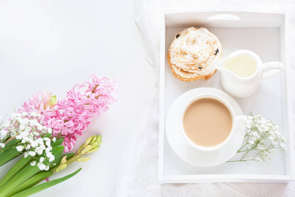 Morning romance breakfast, cup of coffee, milk jug and cake with decor of pink hyacinth. Spring concept. Top view. - 写真・画像