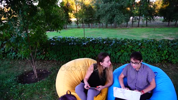 Estudantes universitários encantadores escolhem o tema para escrever apresentação geral, usando tablet e laptop sentados em poltrona ao ar livre no parque à tarde
. - Filmagem, Vídeo