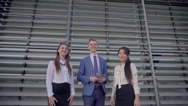 Üç kendine güvenen genç insanlar öğrenciler kağıt dağılım ve gülümseyen ve gülüyor, başarı, iş merkezinin nötr renklerde açık havada duran sevinirler. - Video, Çekim