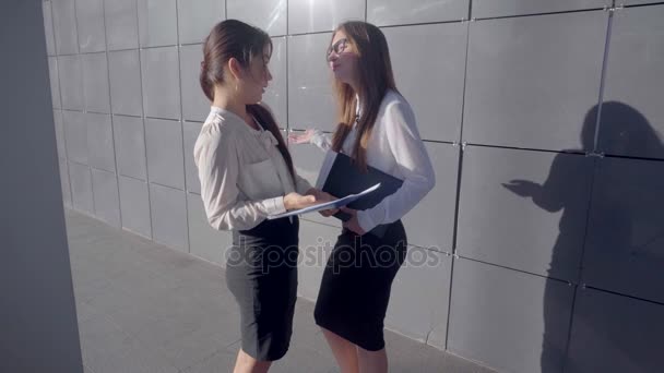 Twee aantrekkelijke jonge vrouwelijke ondernemers te bespreken, bestuderen van documenten en staan op de achtergrond van Business Center buiten in neutrale kleuren. - Video