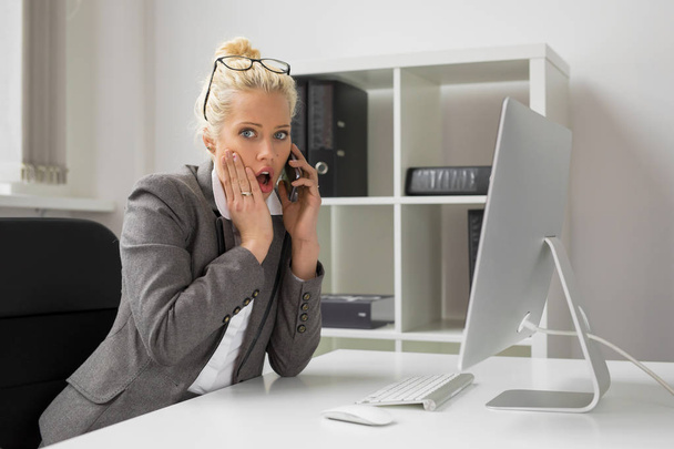 Woman in office talking on the phone and being shocked - Photo, Image