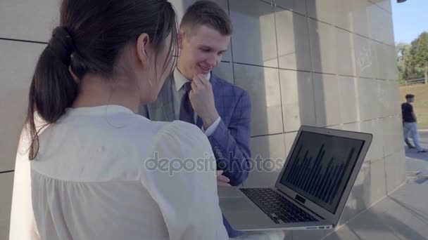 Két lány és egy fiú tart kezében Laptop és mappák, és mosolyogva néz a kamera háttér üzletközpont, szabadban, semleges színek. - Felvétel, videó