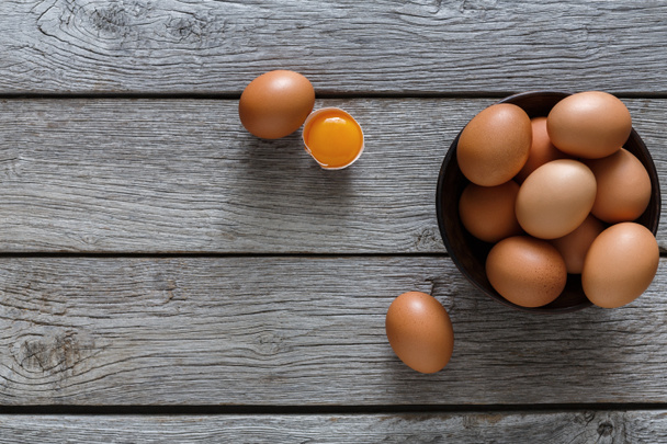 Bruine en witte biologische eieren in kom op houten achtergrond - Foto, afbeelding
