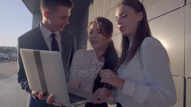 Giovani moderni, due ragazze e ragazzi studiano il computer portatile e parlano con sorridente sullo sfondo del business center all'aperto in colori neutri
. - Filmati, video
