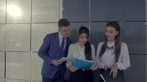 Grupa młodych profesjonalistów inteligentne rozmowy, trzymając w rękach papieru i zobaczyć je, na tle ściany z centrum biznesowe poza w neutralnych kolorach. - Materiał filmowy, wideo