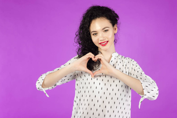 young curly brunette woman making a hand heart frame on a pink b - Foto, imagen