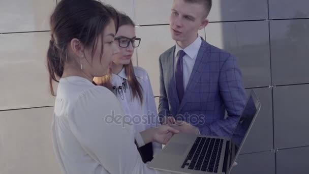 Uczniowie dwie dziewczyny i chłopak trzymają w rękach gadżet i foldery na tle Business Center na zewnątrz w neutralnych kolorach. - Materiał filmowy, wideo
