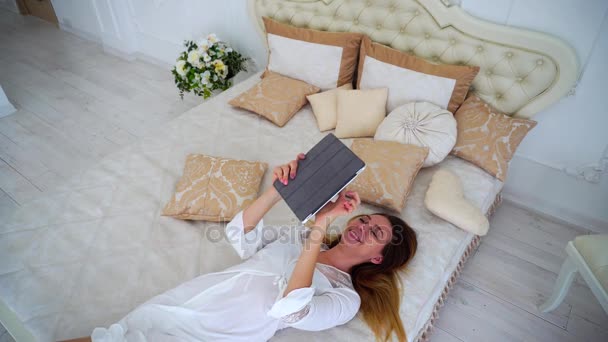 Fiatal nő megpróbál minket szerkentyű és olvas Hírek a nap Internet ágyon fehér hálószoba. - Felvétel, videó