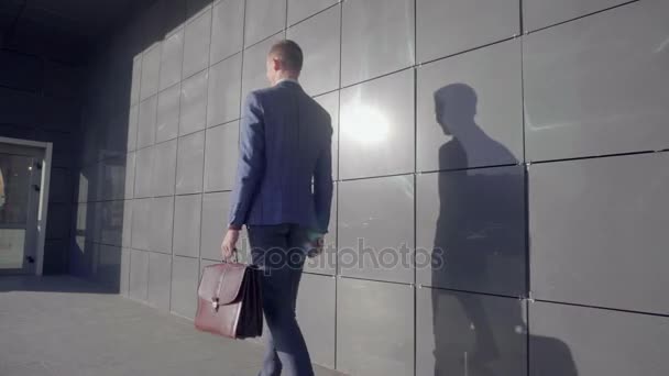 Επαγγελματίες νεαρός επιχειρηματίας πηγαίνει κατά μήκος και κοιτάζει το ρολόι στο φόντο του επιχειρηματικού κέντρου σε εξωτερικούς χώρους σε ουδέτερα χρώματα. - Πλάνα, βίντεο