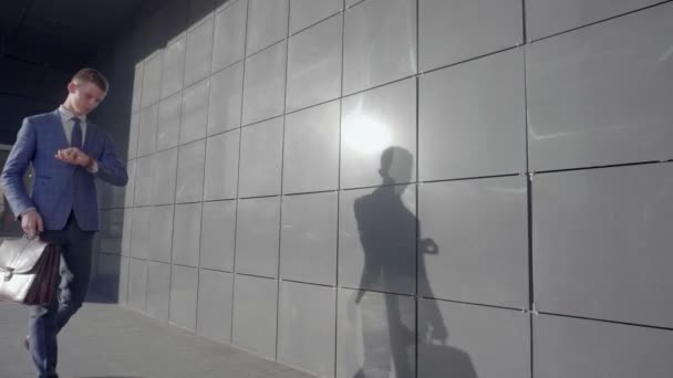 Fiatal férfi Manager séta és néz óra kezét, háttérben a Business Center, szabadban, semleges színek. - Felvétel, videó