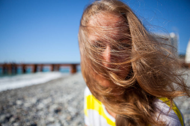 Mooie meisje in zonnige zomerdag op straat in de buurt van de zee. Een sterke wind berm de haarstijl - Foto, afbeelding