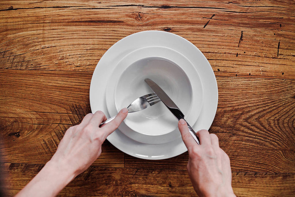 Κάτοψη της γυναίκας χέρια κρατώντας μαχαίρι και πιρούνι σε ξύλινο τραπέζι - Φωτογραφία, εικόνα