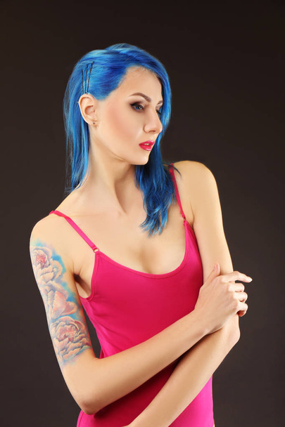 Hermosa mujer joven con pelo de color elegante y tatuaje sobre fondo oscuro
. - Foto, Imagen