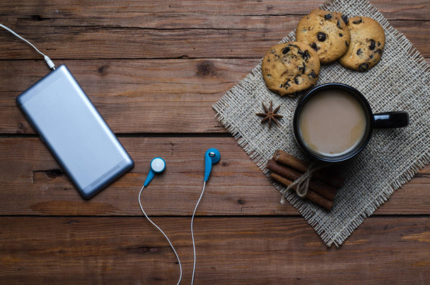 A smartphone with headphones and a cup of coffee on a wooden tab - Foto, imagen