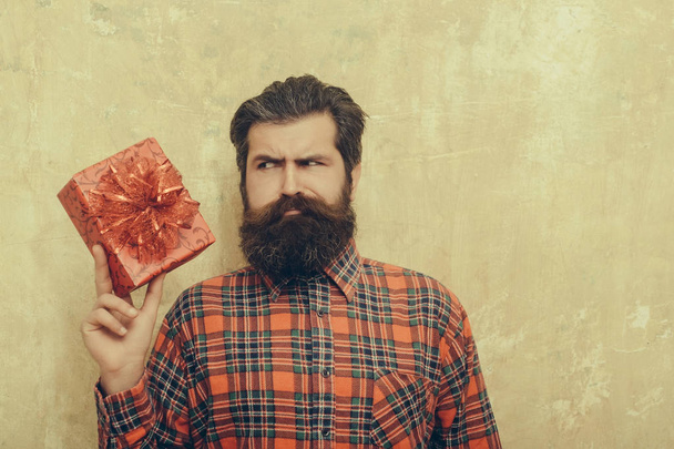 θλιβερή γενειοφόρος άνδρας με κόκκινο δώρο κουτί με φιόγκο - Φωτογραφία, εικόνα