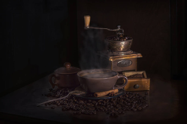 Naturaleza muerta con granos de café, un molinillo de café viejo y una taza de café caliente
 - Foto, Imagen