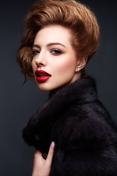 Young girl in a fur coat and bright makeup. Beautiful model with red lips and hairstyle - Foto, afbeelding