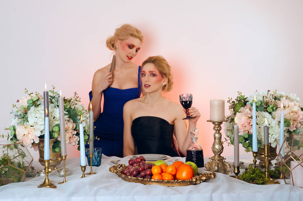 Twee fashion modellen achter de tafel met vruchten, kaarsen en win - Foto, afbeelding