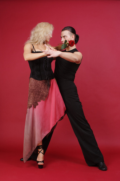 Beautiful blond and brunet with rose in teeth dancing tango on red background - Φωτογραφία, εικόνα