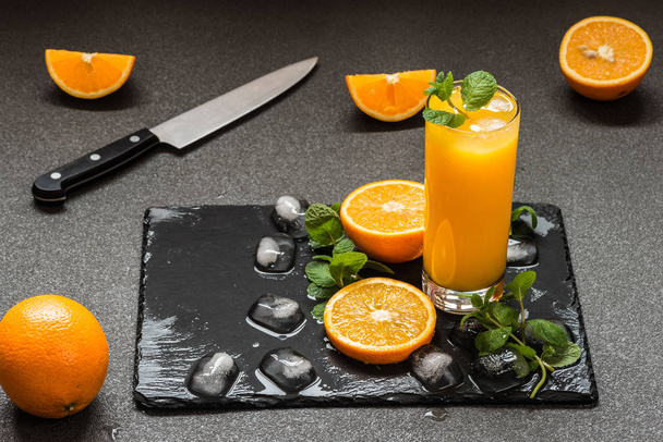 jus d'orange en verre près d'agrumes, glace et menthe sur fond sombre
 - Photo, image