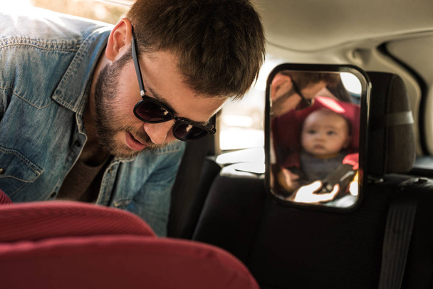 Pai prenda seu bebê no assento do carro
 - Foto, Imagem