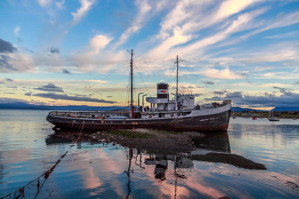 Velho barco a vapor quebrado encalhado em terra em uma luz do pôr do sol, Ushuaia
 - Foto, Imagem