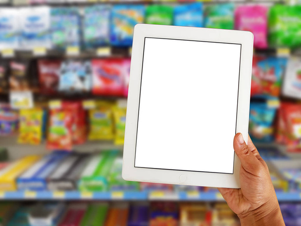 asiatique droite tenant écran tablette vierge sur flou divers marque de bonbons dans l'emballage à vendre sur le stand de supermarché ou étagère
  - Photo, image