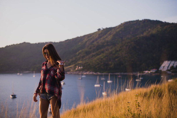 A girl stands on the edge of the cliff near the sea or ocean and looking at the sun valley. Woman enjoying a sunset or sunrise from the top of the mountain. The traveler girl see the sunrise at the - Foto, Bild