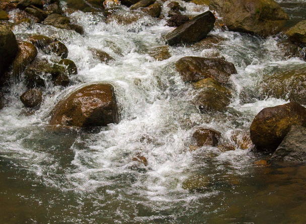 Fresh water river among black rocks. Fresh aqua fast stream in stones. - Fotó, kép