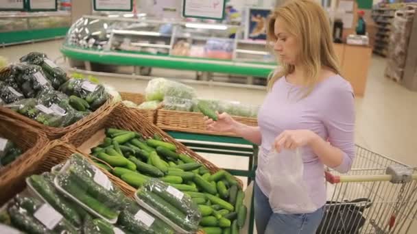 A woman in a supermarket on a vegetable shelf, buying vegetables . Cucumber - Кадри, відео