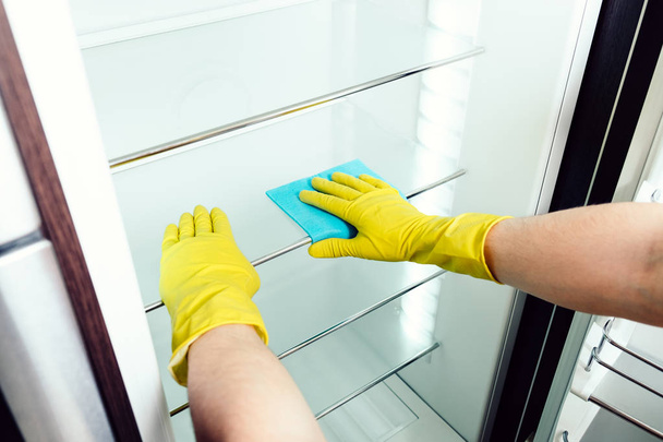 Man's hand cleaning white fridge with blue rag - Фото, изображение