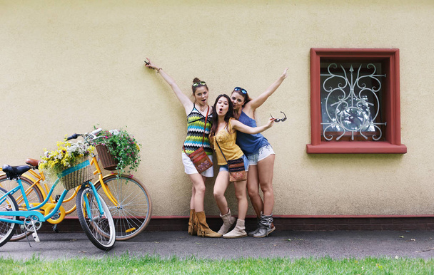 Happy boho chic girls pose with bicycles near house facade - Photo, Image