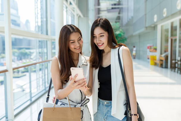 Женщины ходят по магазинам и смотрят на смс-ки со смартфонов
 - Фото, изображение