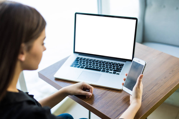 Üstten Görünüm, yakın-up ile laptop ile yuvarlak tahta masada oturan genç kadının elinde boş perde smartphone - Fotoğraf, Görsel