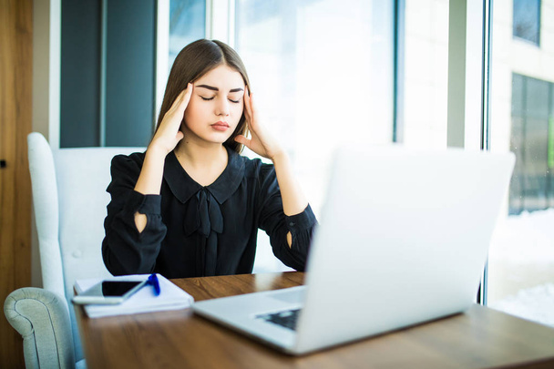 Втомилася від болю в голові жінка думає про те, як виконати завдання на ноутбуці за столом
 - Фото, зображення