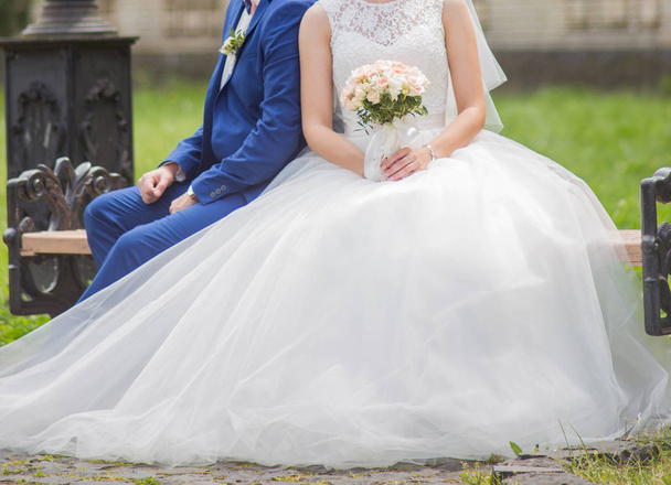 The bride and groom sit on a bench in the park - Foto, imagen