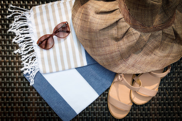 Concept of flat lay summer accessories of white, blue and beige Turkish towel, sunglasses and straw hat on rattan lounger with blue swimming pool as background. - Photo, Image