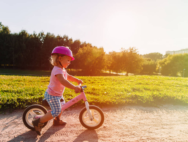 little girl with helmet riding bike at sunset - Fotoğraf, Görsel