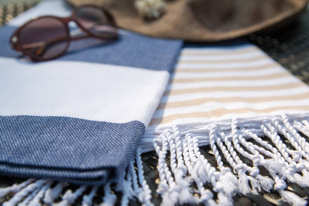 Conceito de acessórios de verão close-up de branco, azul e bege toalha turca, óculos de sol e chapéu de palha na espreguiçadeira de vime
. - Foto, Imagem