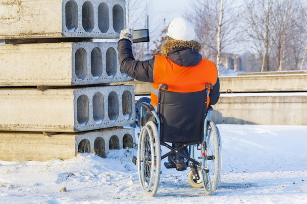 Инвалид в инвалидной коляске фотографирует на планшете на стройплощадке
  - Фото, изображение