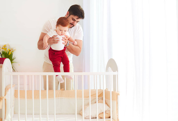 happy father putting the infant baby in the cot at home - Photo, Image