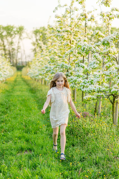 Una hermosa niña corre a través de un jardín floreciente en el s
 - Foto, Imagen