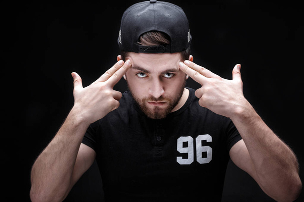 portrait of handsome young man in black shirt and cap on black background. rapper - Фото, изображение