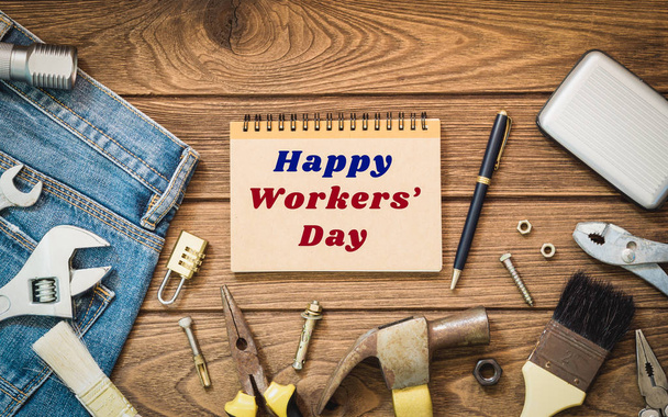 国際的な労働者の日背景コンセプト - ジーンズ、多くの便利なツール、幸せな労働者の日本文、木製の背景トップ ビュー ノートブック  - 写真・画像