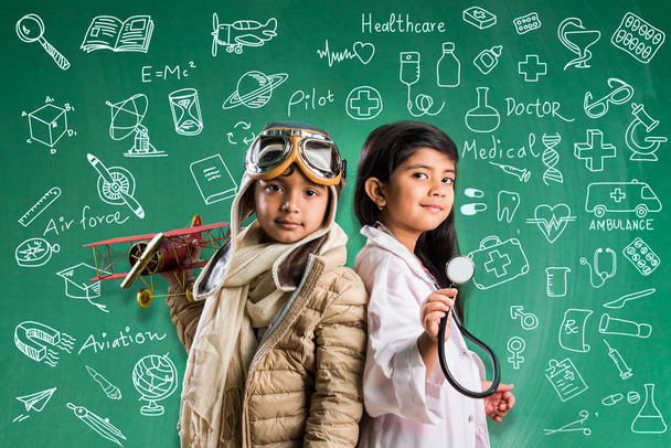 Lapset ja koulutus käsite Pieni intialainen poika ja tyttö poseeraa edessä Green liitu aluksella doodles pilotti fancy mekko ja lääkäri puku stetoskooppi, haluavat olla lentäjä tai lääkäri
 - Valokuva, kuva