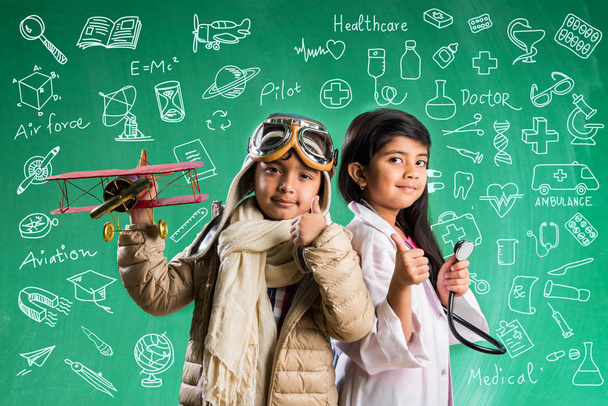 Kinder und Bildungskonzept - kleine indische Jungen und Mädchen posieren vor grünem Kreidebrett mit Kritzeleien in Pilotenkleidung und Arztkostüm mit Stethoskop, wollen Pilot oder Arzt werden - Foto, Bild