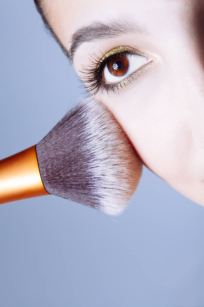  Face of young woman getting powder on her cheek with a brush. - Foto, imagen